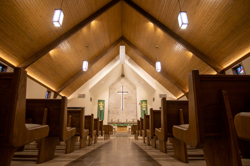The center aisle of the Hope Lutheran church. Lined with pews. Leading to the alter and illuminated cross.